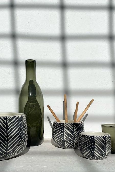 Set of ceramic bowls including a bottle, cups, and a holder with wooden sticks on a light surface.
