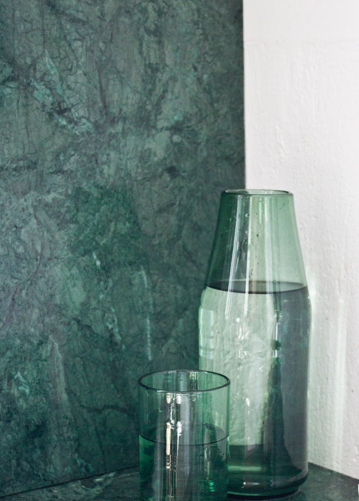 Green glass carafe next to a green glass filled with water posed on a green marble