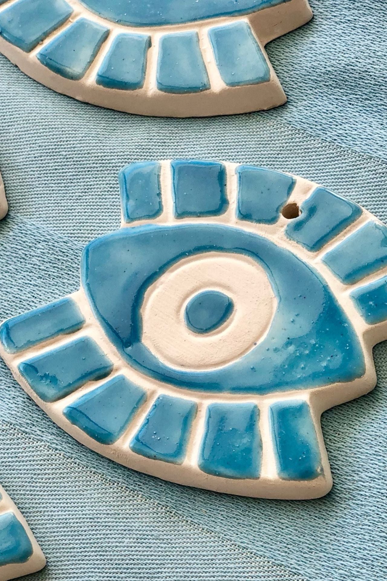 Ceramic eye-shaped ornament with blue and beige design on a textured blue surface