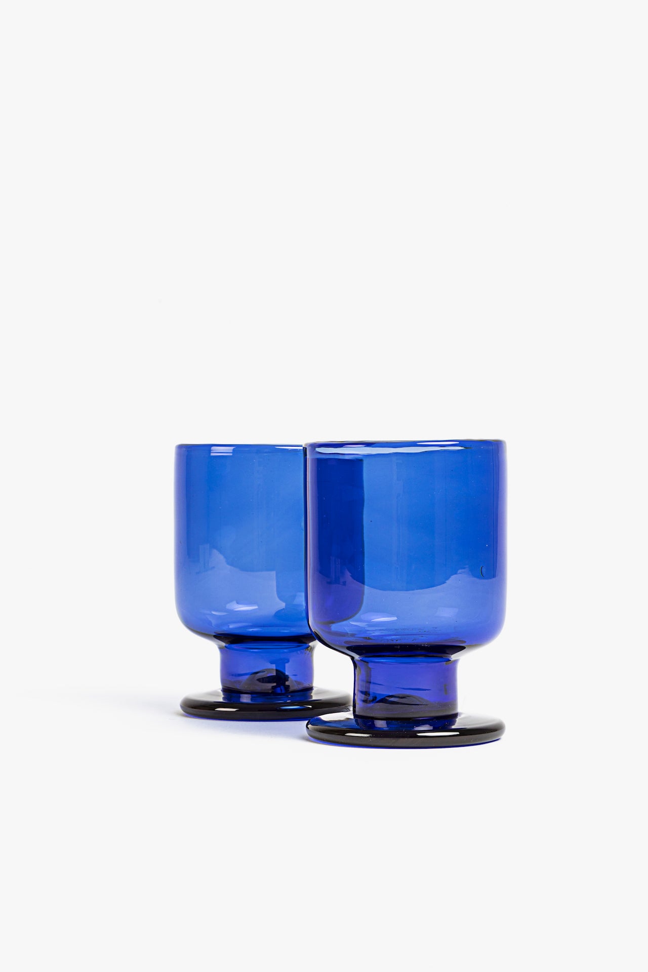 Two blue blown glass tumblers on a white background