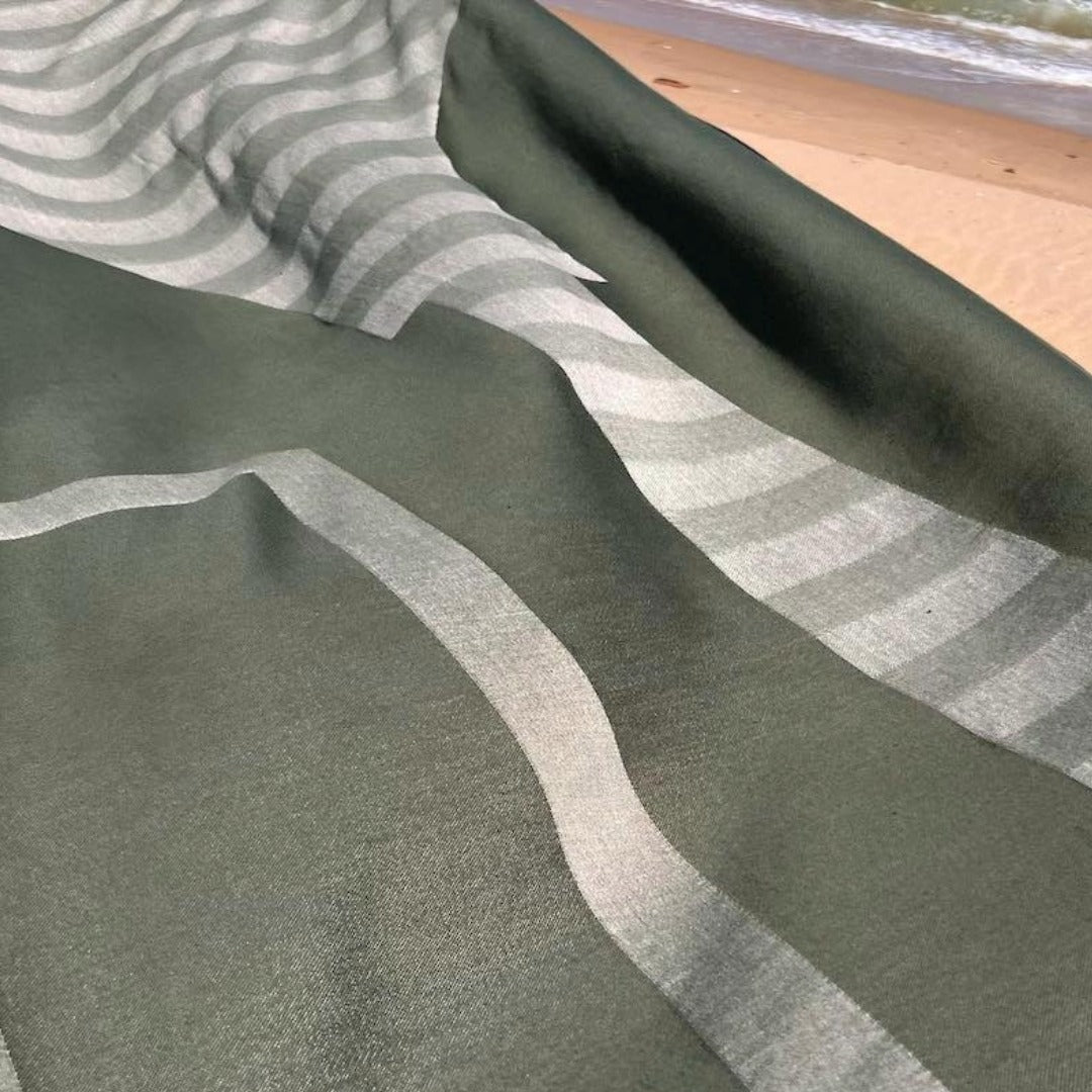 Close-up of olive green fabric with stripes on a beach.