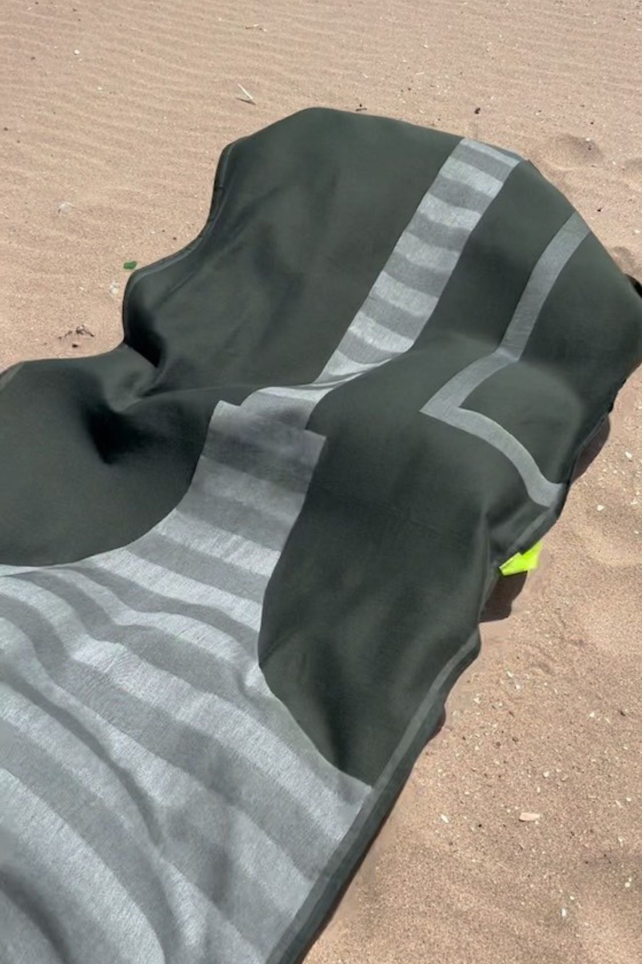 Green and gray fouta towel on a sandy surface